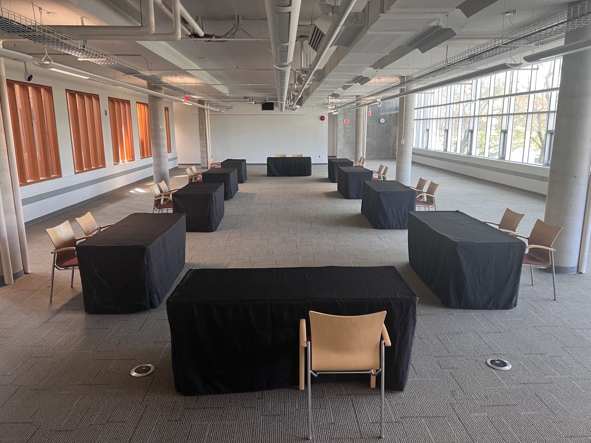 Empty meeting room with spaced black-covered tables and chairs in a bright carpeted hall
