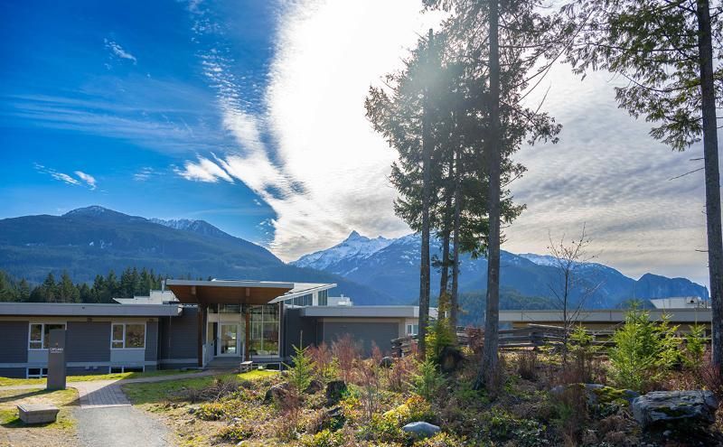 A modern, low-slung building with a mountain backdrop, under a sunny sky.