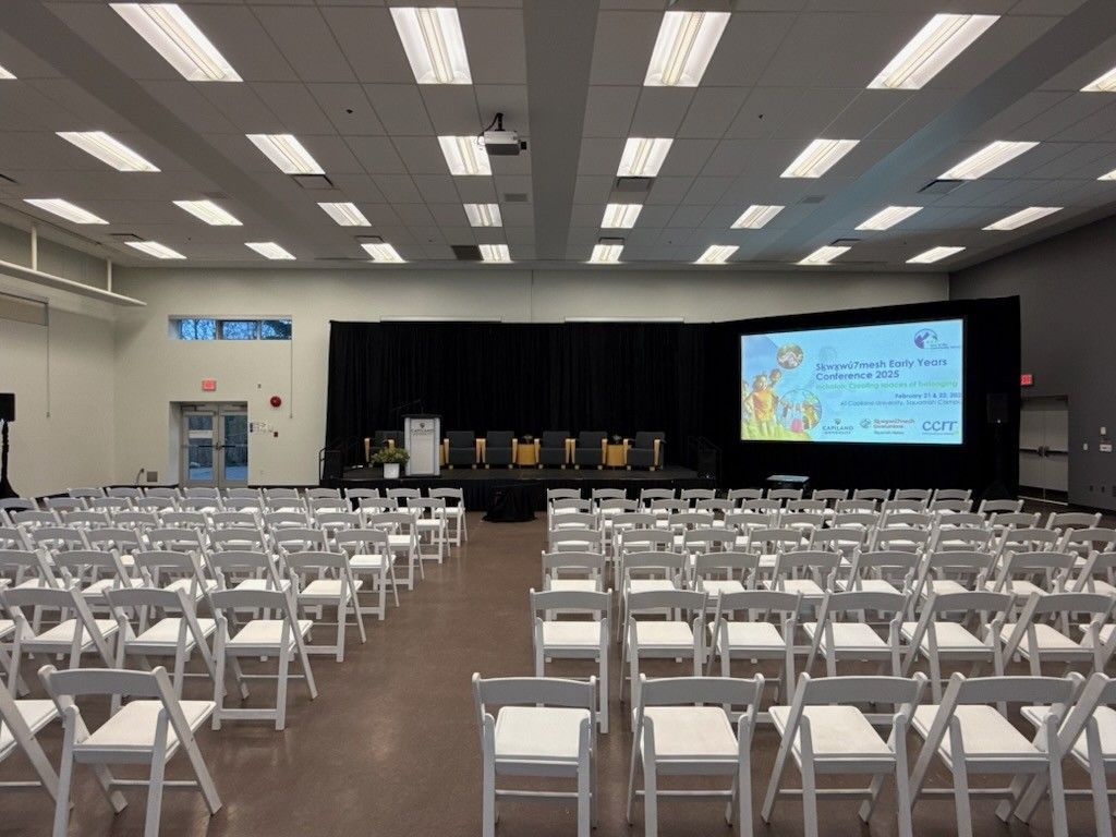 Empty conference hall with rows of white folding chairs facing a stage and large presentation screen