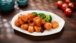 White plate of crispy glazed chicken with broccoli on a dark wooden table
