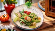 White bowl of fresh vegetable salad with peppers, asparagus, and scallops on a wooden table