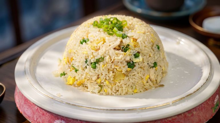Plate of fried rice on a white dish, topped with green herbs, on a restaurant table