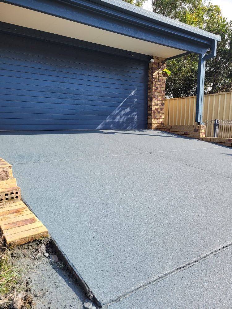 A Blue Garage Door With a Concrete Driveway in Front of It — Mid North Coast Spray Pave in Port Macquarie, NSW