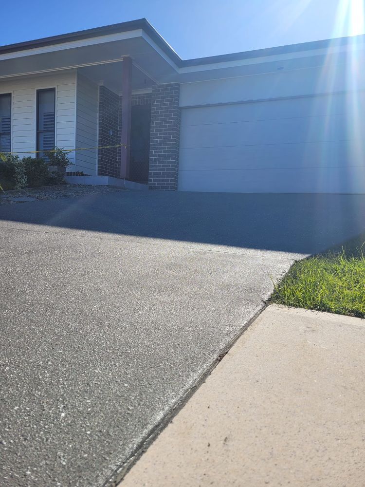 A White House With a White Garage Door is Sitting Next to a Sidewalk — Mid North Coast Spray Pave in Port Macquarie, NSW