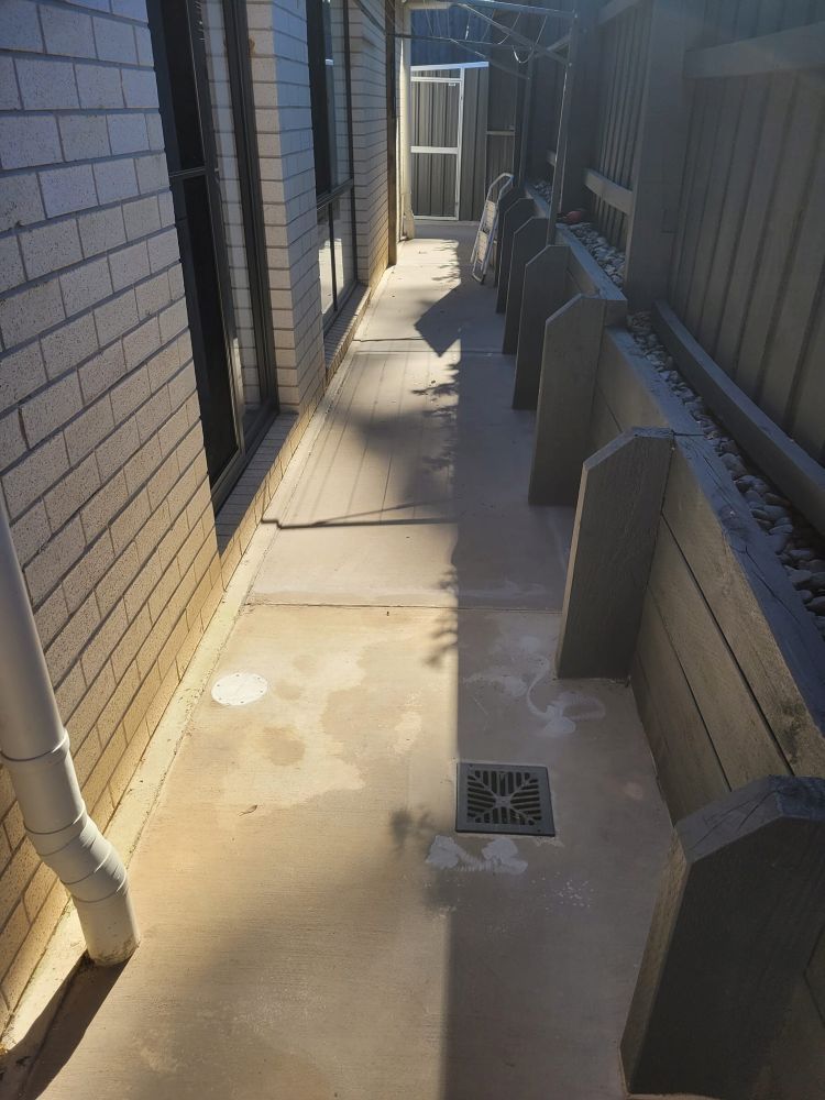 A concrete walkway between two brick buildings with a drain in the middle.