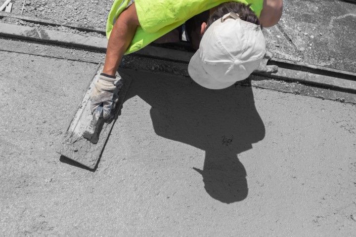 Worker in a white hard hat smoothing gray concrete with a trowel.