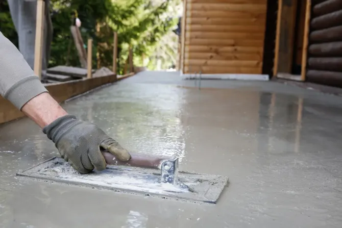 Gloved hand smoothing wet concrete on an outdoor patio near a wooden structure