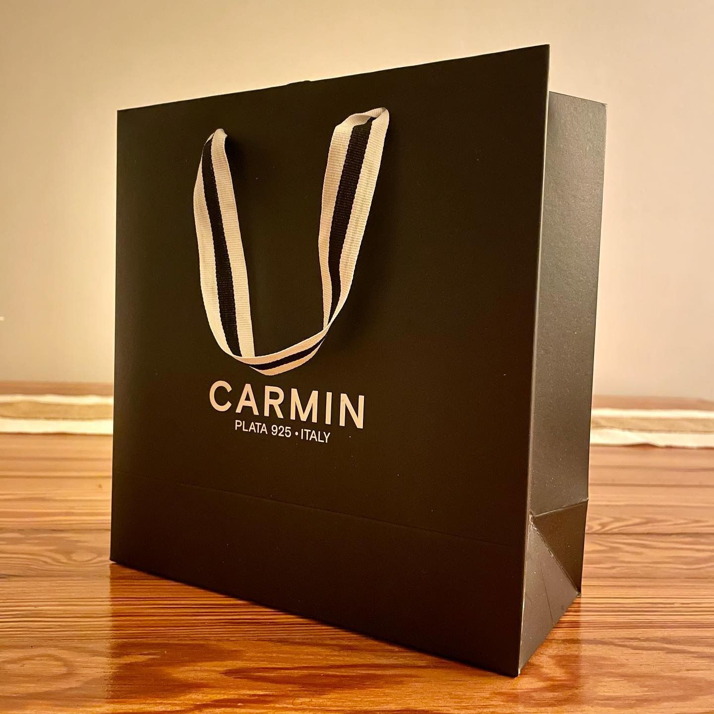 Bolsa de compras CARMIN negra con asas de cuerda blanca sobre una superficie de madera.