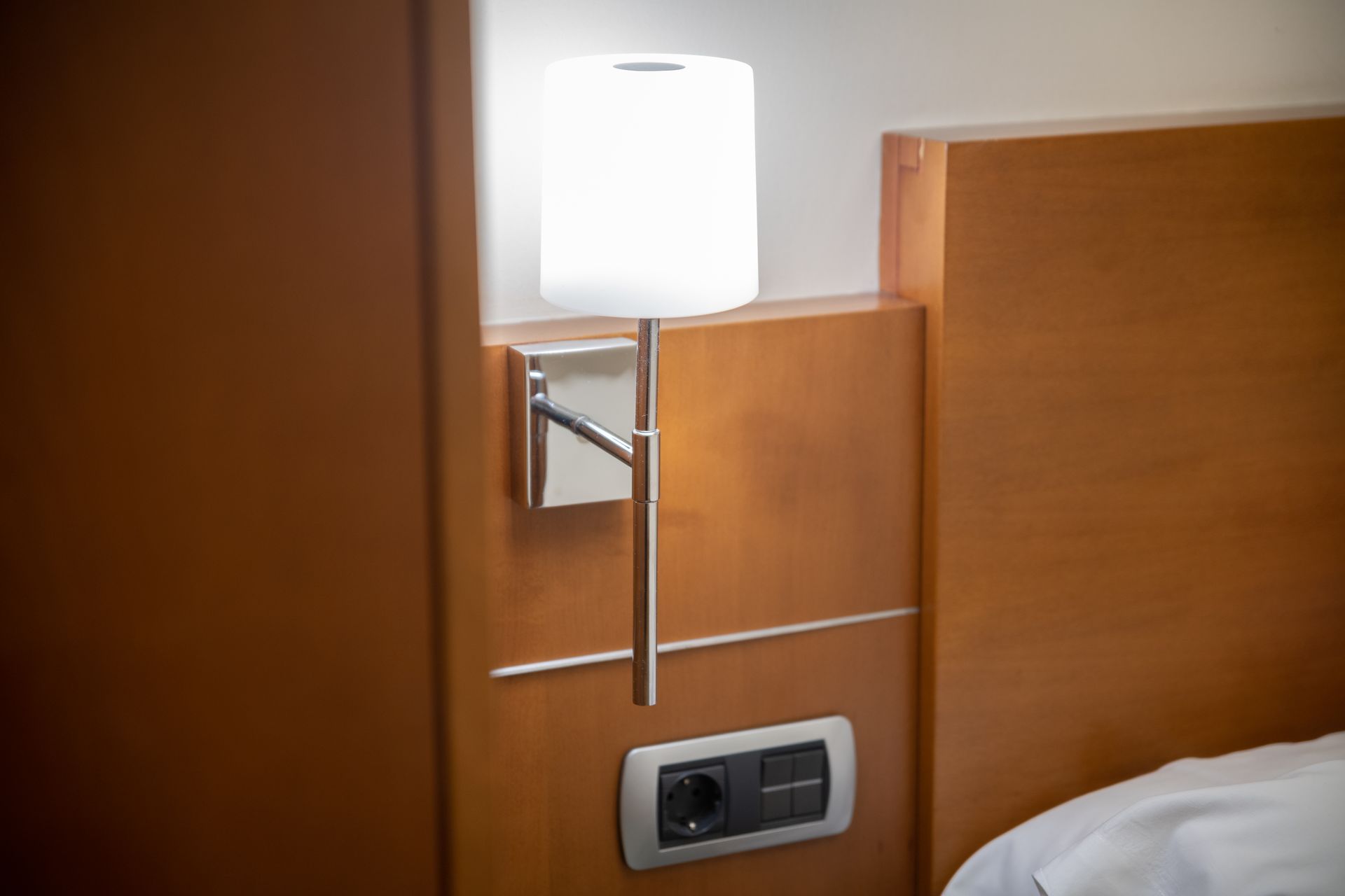 Lámpara de mesita de noche del hotel, cabecero de madera y enchufe junto a la cama.