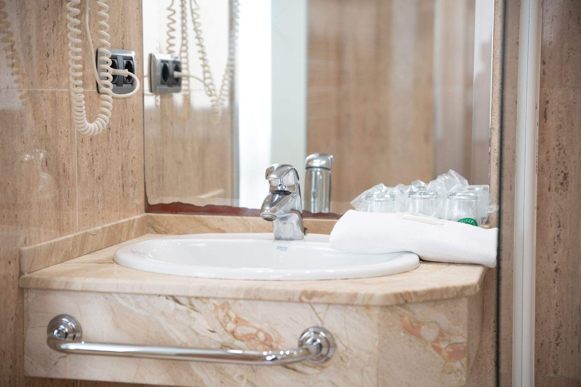 Lavabo de mármol con grifo cromado, teléfono de pared con cable colgante y una toalla doblada cerca