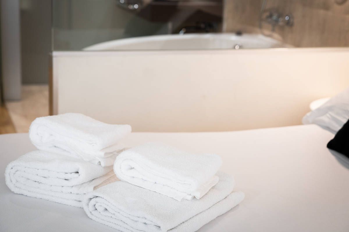 Toallas blancas apiladas sobre la encimera del baño junto a un lavabo, con una bañera al fondo