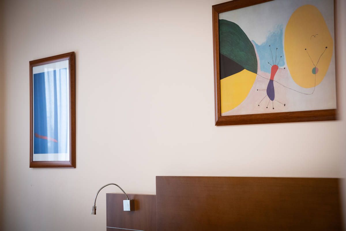 Pared de habitación de hotel con una obra de arte abstracta enmarcada, una lámpara y un cabecero de madera