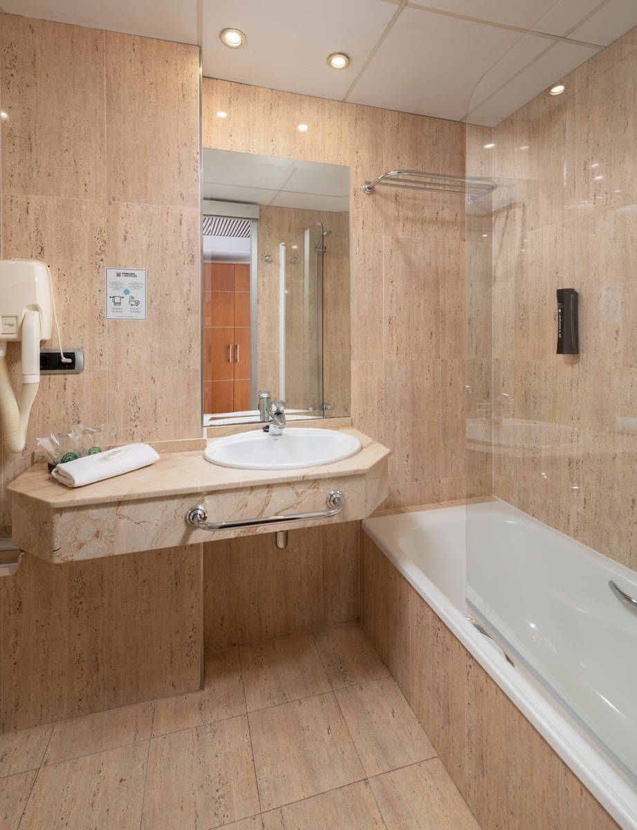 Baño moderno con azulejos beige, lavabo, espejo y bañera.