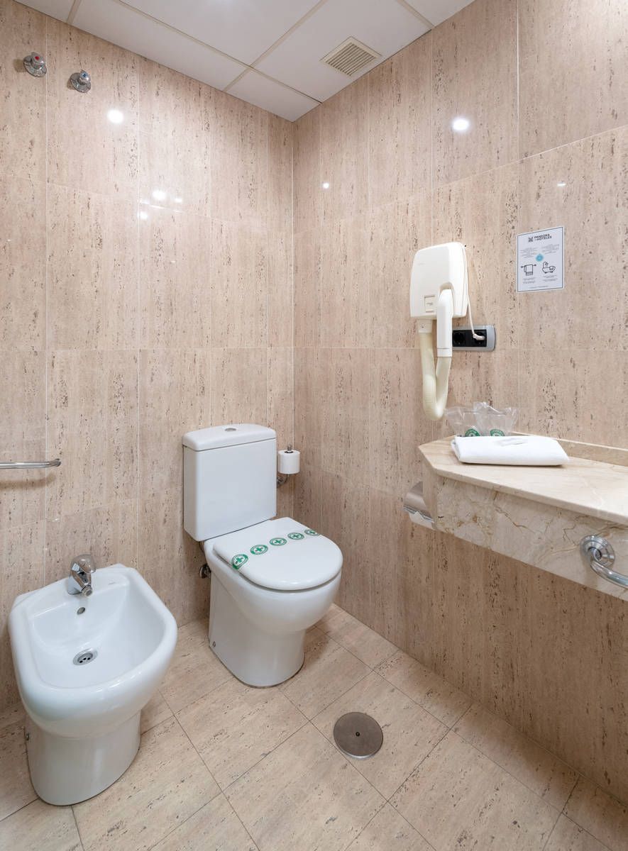 Baño accesible con bidé, inodoro, lavabo y secador de manos de pared, con azulejos beige