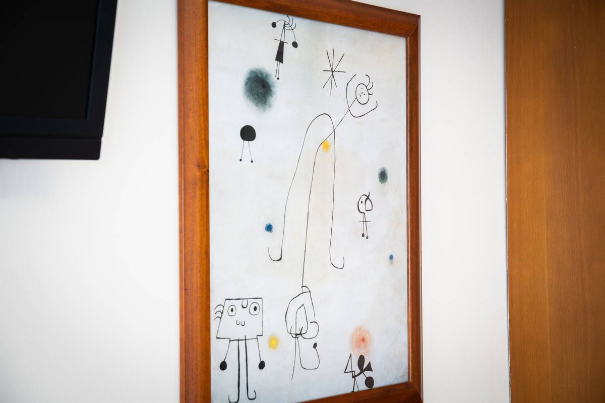 Arte abstracto de garabatos enmarcado en una pared blanca, con trazos negros, amarillos y naranjas.