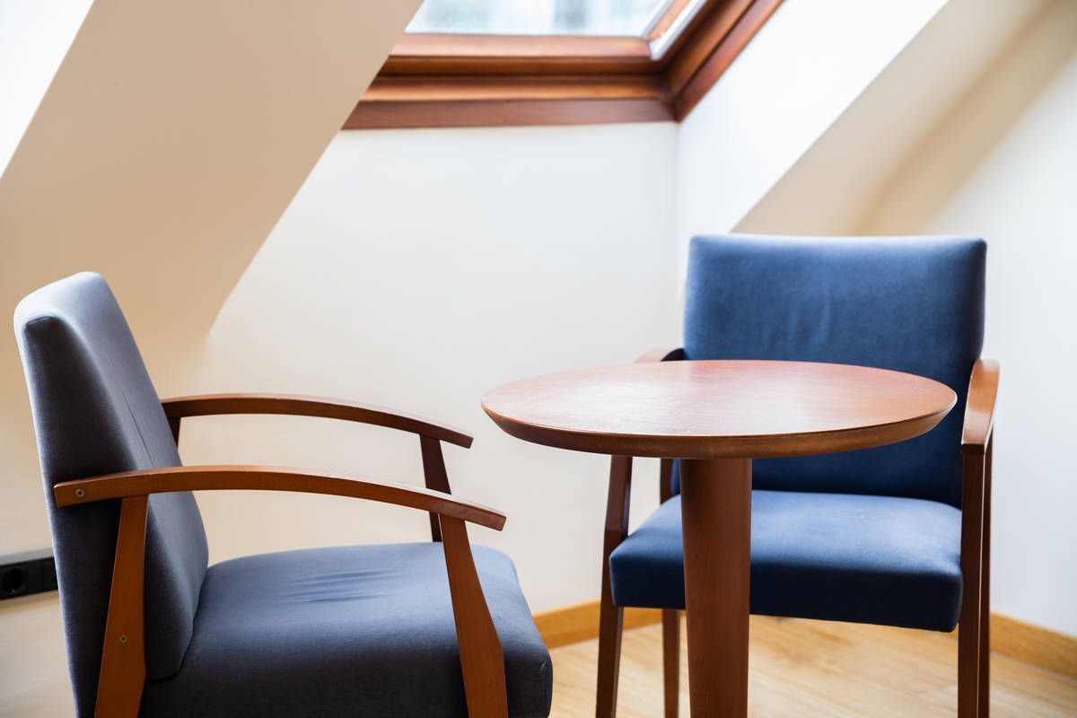 Dos sillas azules y una mesa redonda de madera junto a una claraboya, en una habitación luminosa