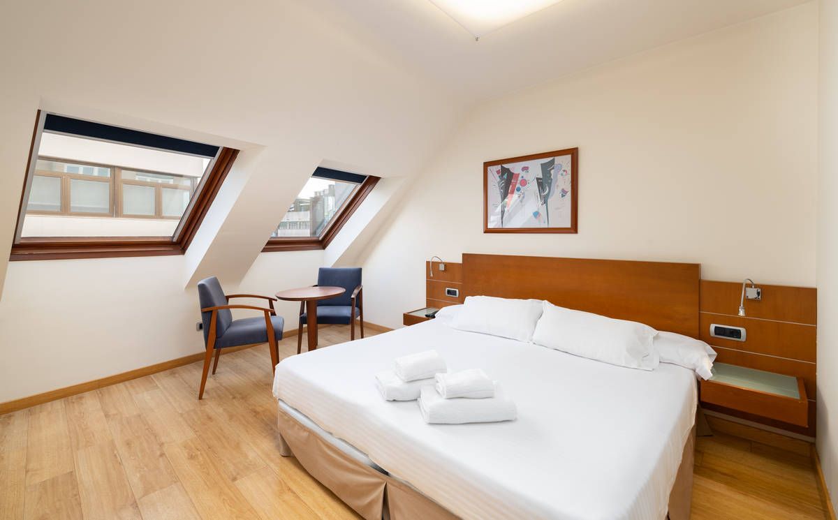 Luminoso dormitorio abuhardillado con cama doble, muebles de madera y ventanas en el techo
