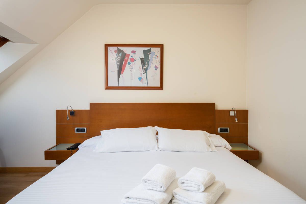 Dormitorio luminoso con una cama blanca perfectamente tendida, un cabecero de madera y un mapamundi enmarcado sobre la cama.