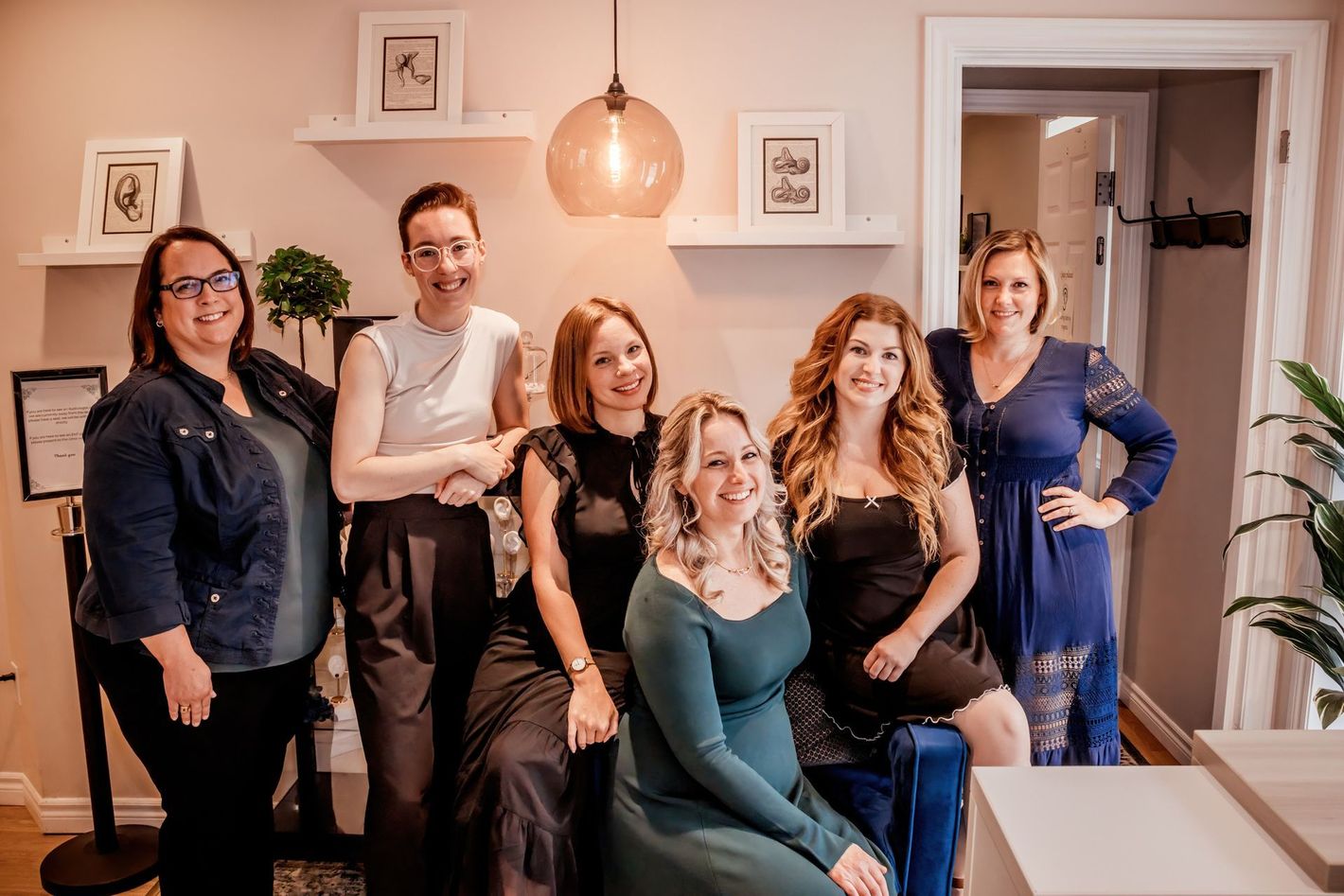 Six people posing together in a cozy room with shelves, framed art, and warm lighting