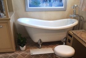 Clawfoot bathtub in bathroom with stone floor, small plants, a stool, and framed artwork.