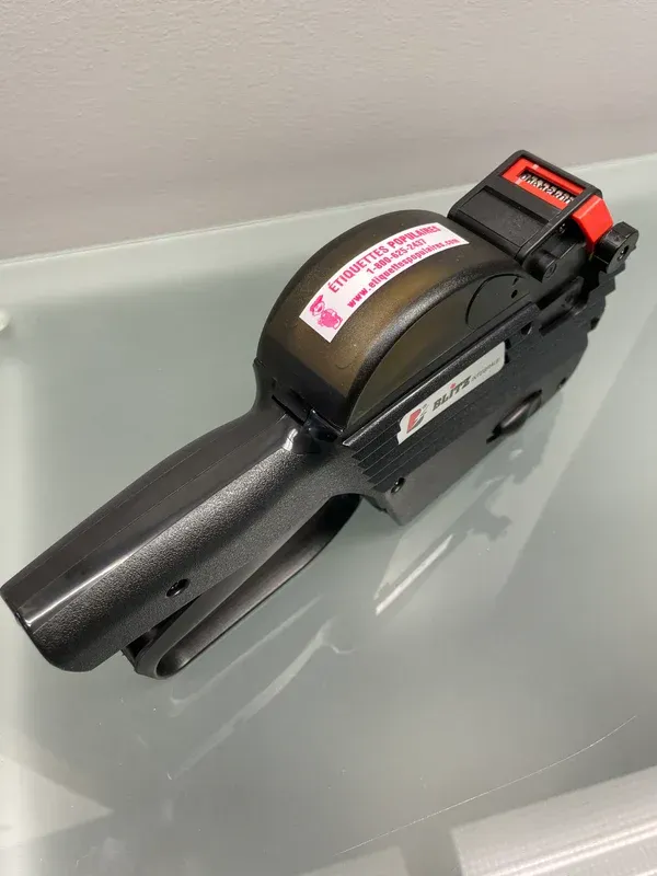 Pistolet étiqueteur noir sur une surface réfléchissante avec une étiquette rose.