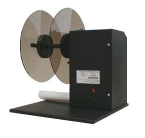 Distributeur d'étiquettes avec deux disques transparents bruns et un rouleau d'étiquettes blanches. Socle et boîtier noirs.