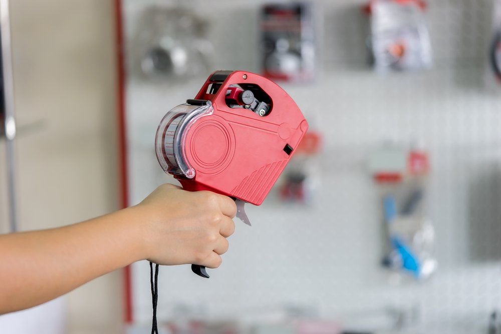 Main d'une personne tenant un pistolet à étiquettes de prix rouges dans un magasin.