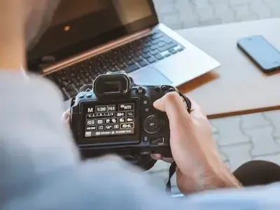 A person is holding a camera in front of a laptop.