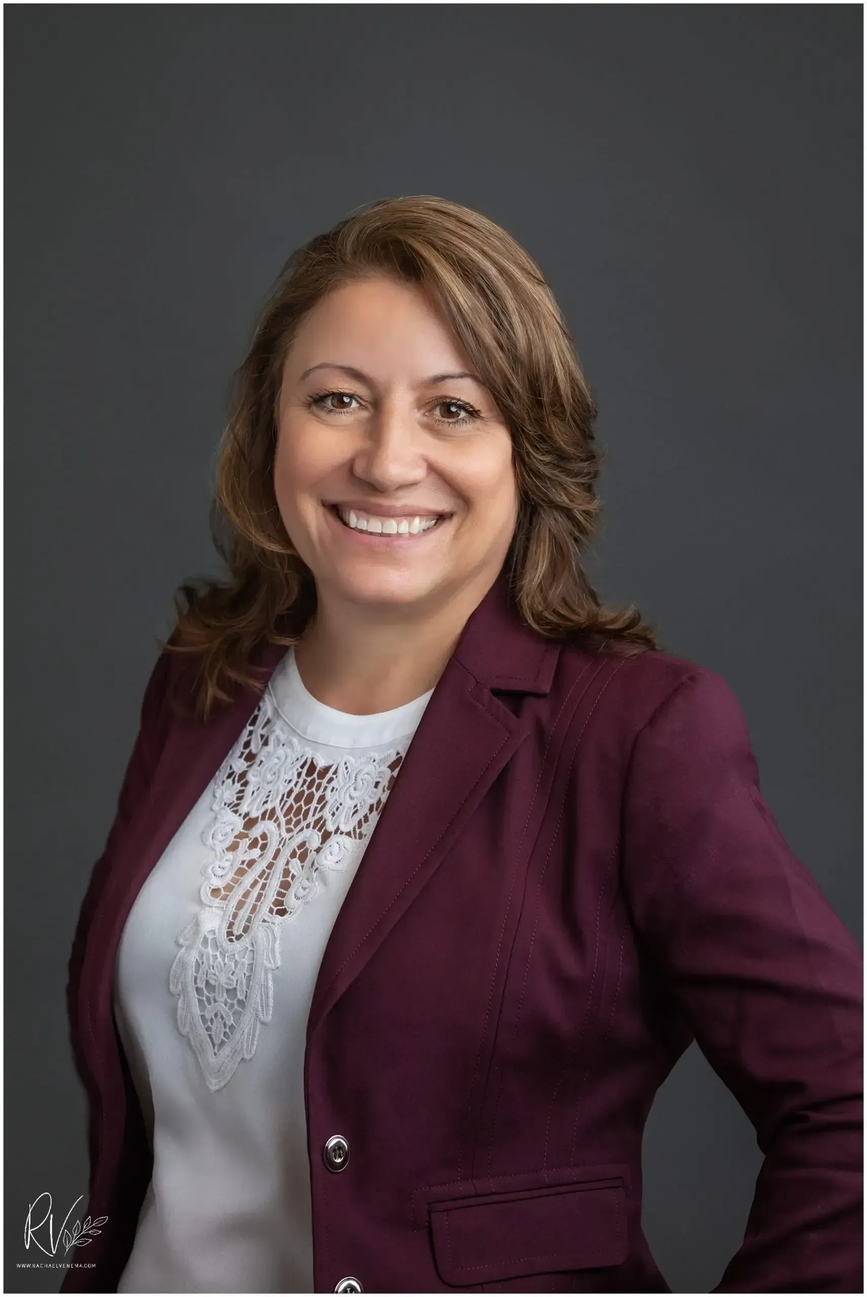 A woman in a purple jacket and white shirt is smiling for the camera.