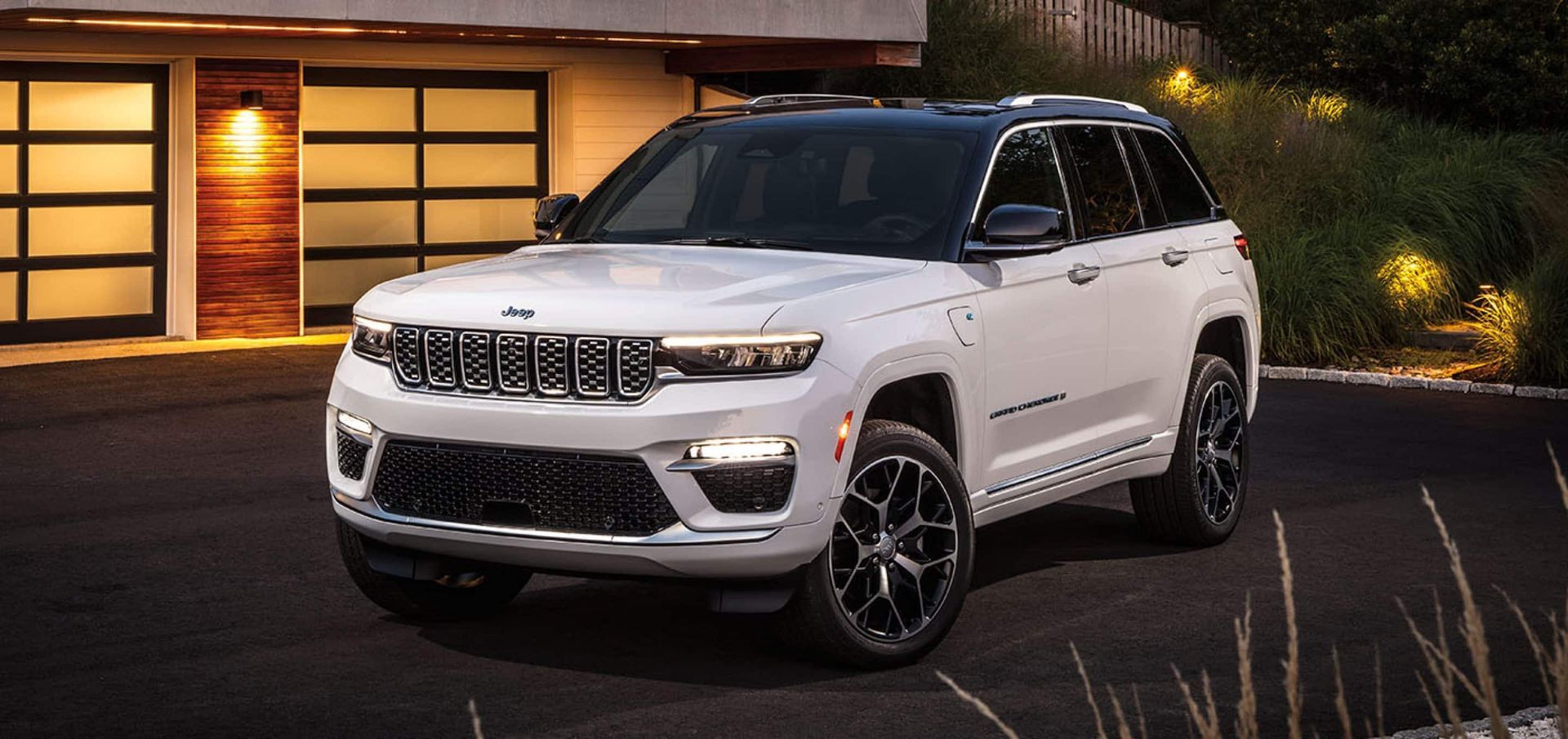 A white jeep grand cherokee is parked in front of a garage.