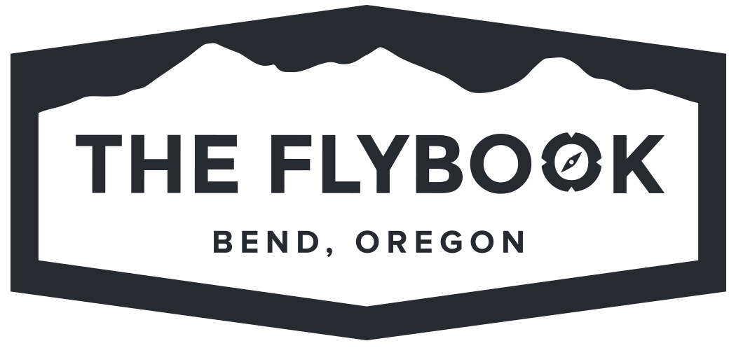 Logo for The Flybook in Bend, Oregon: dark gray emblem with mountains, text, and compass.