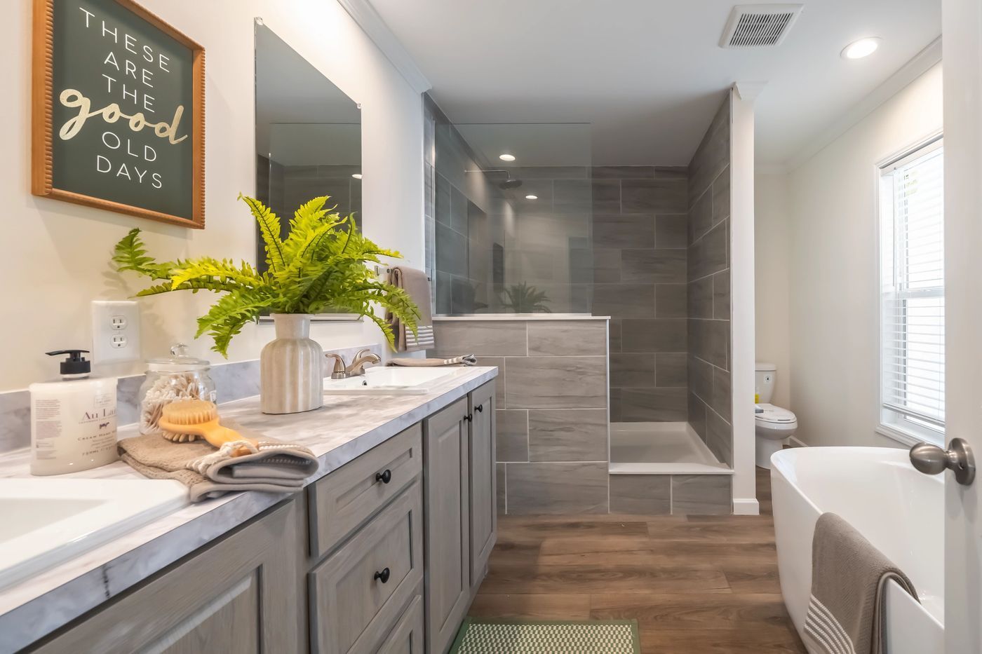 Bathroom with double vanity, shower, freestanding tub, and window. Gray and white color scheme.