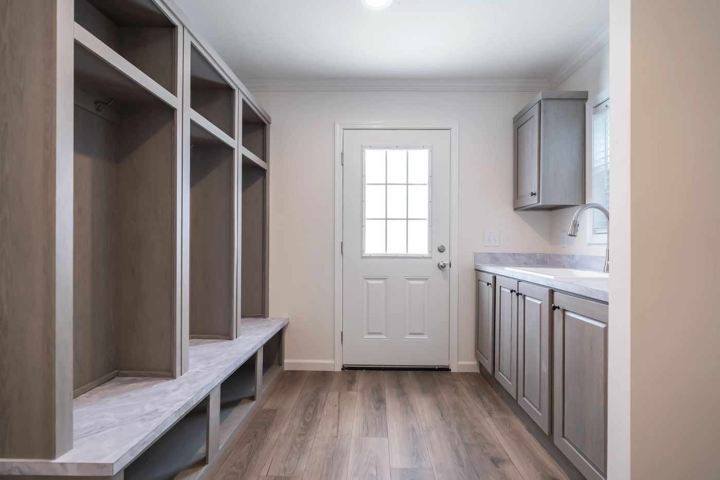 Mudroom with built-in storage, gray cabinets, and a door leading outside, with wood-look flooring.