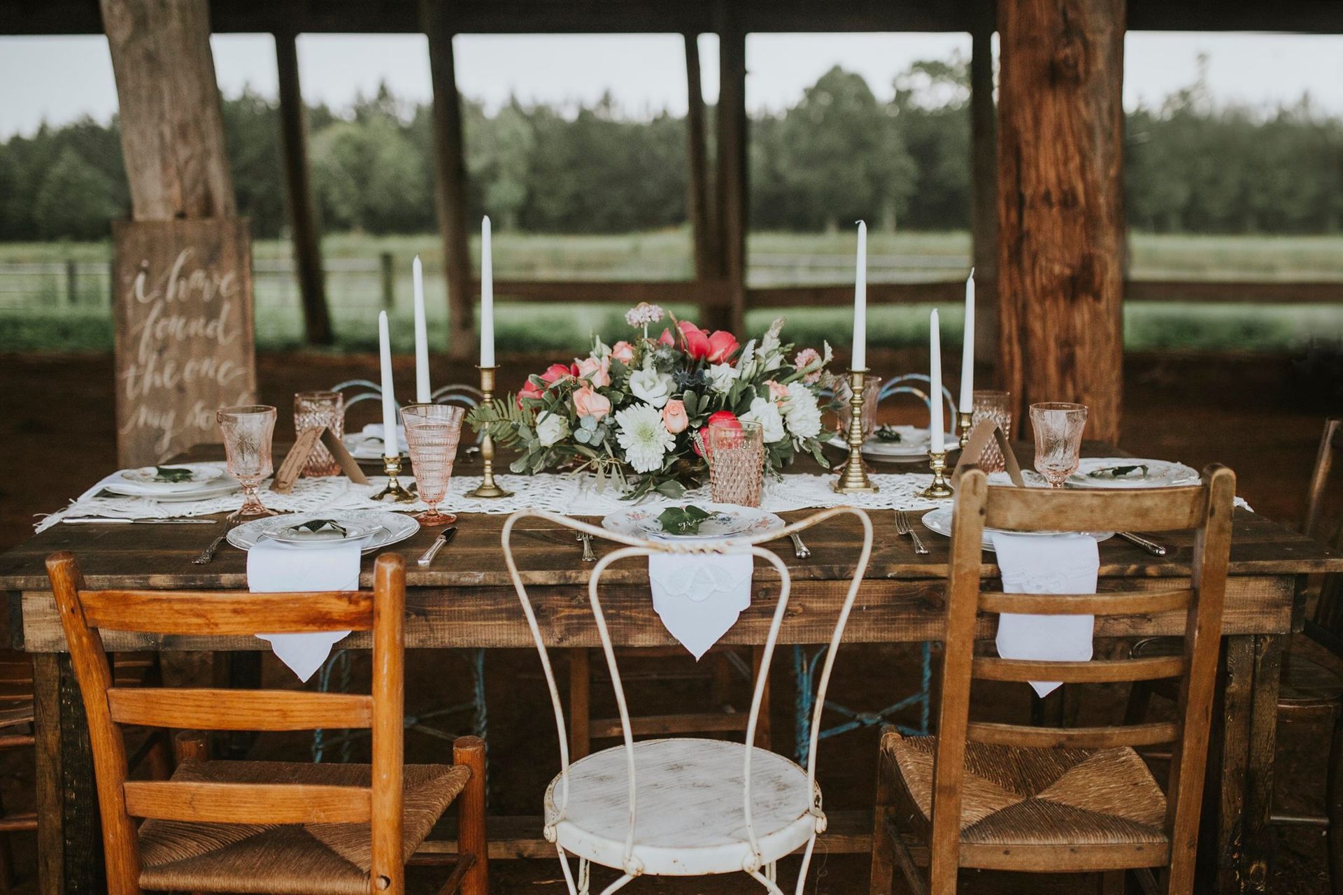 Wedding reception table set with floral centerpiece, candles, and mismatched chairs.