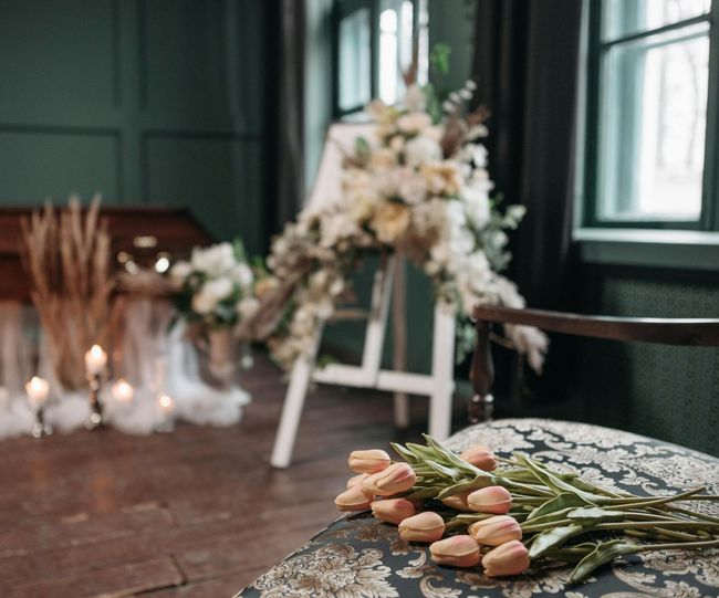 Close-up of pink tulips on a patterned chair. In the background, a floral arrangement and candles.