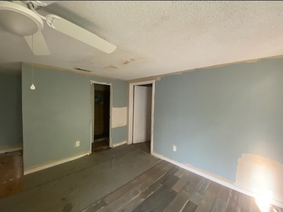 Empty room with blue walls, white ceiling fan, and unfinished flooring. Two doorways are visible.