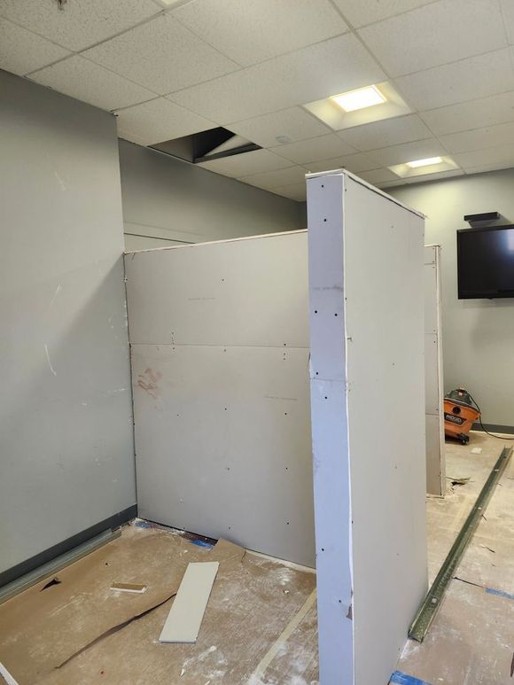 Construction site: Drywall walls being installed, partially enclosing a space, with tools and debris visible.