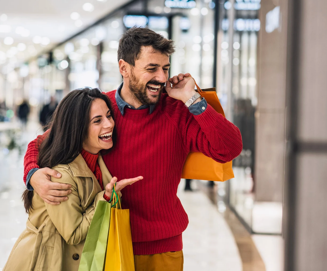 A man is talking on a cell phone while standing next to a woman in a shopping mall.