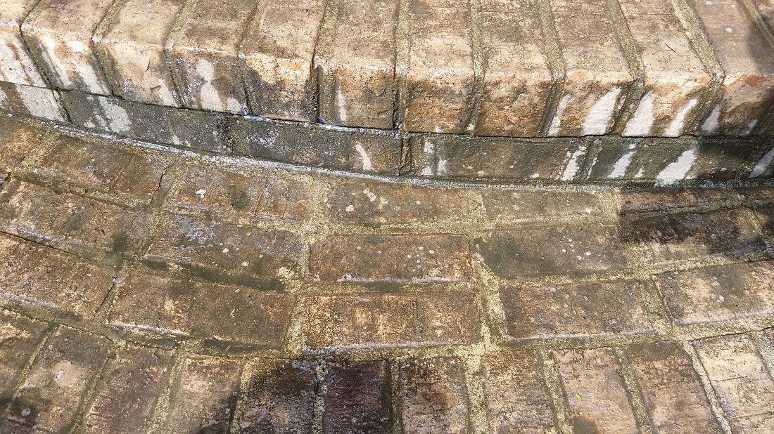An outdoor view of aged, stained brick stairs and a paved walkway with dark discoloration and dirt buildup.