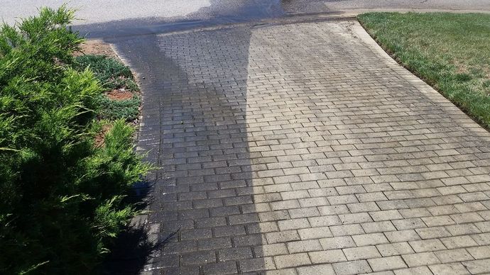 A driveway shows a side-by-side contrast between a clean, light-colored brick section and a dark, stained portion.