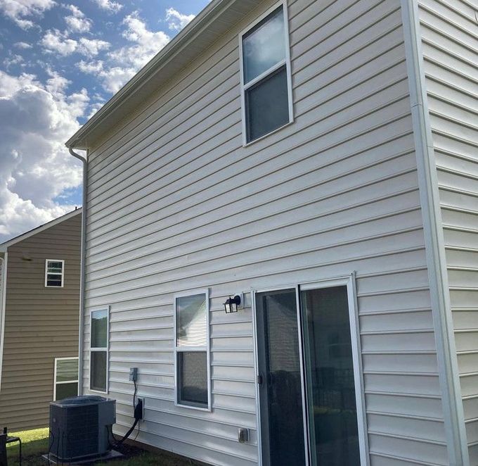 A low-angle view of the cream-colored vinyl siding of a two-story house with a sliding door, windows, and an AC unit.