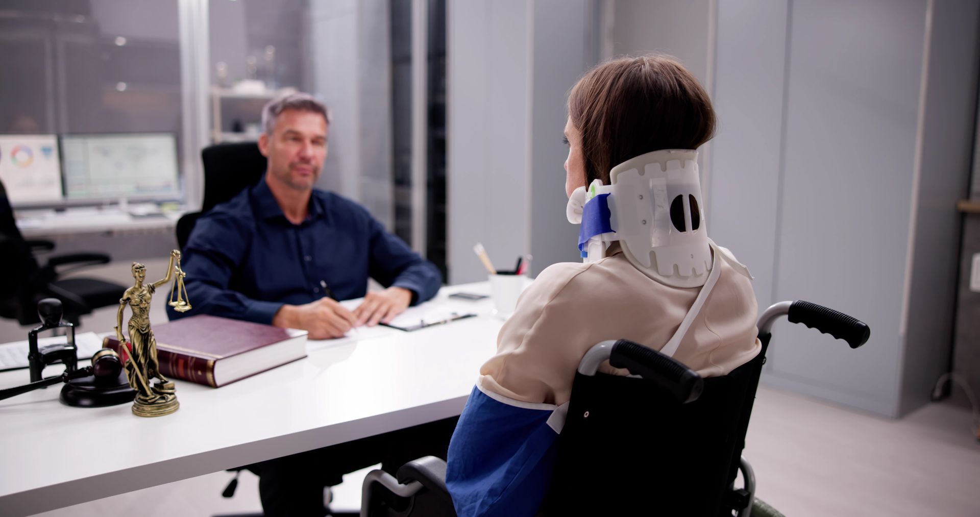A woman in a wheelchair is sitting at a desk talking to a lawyer.