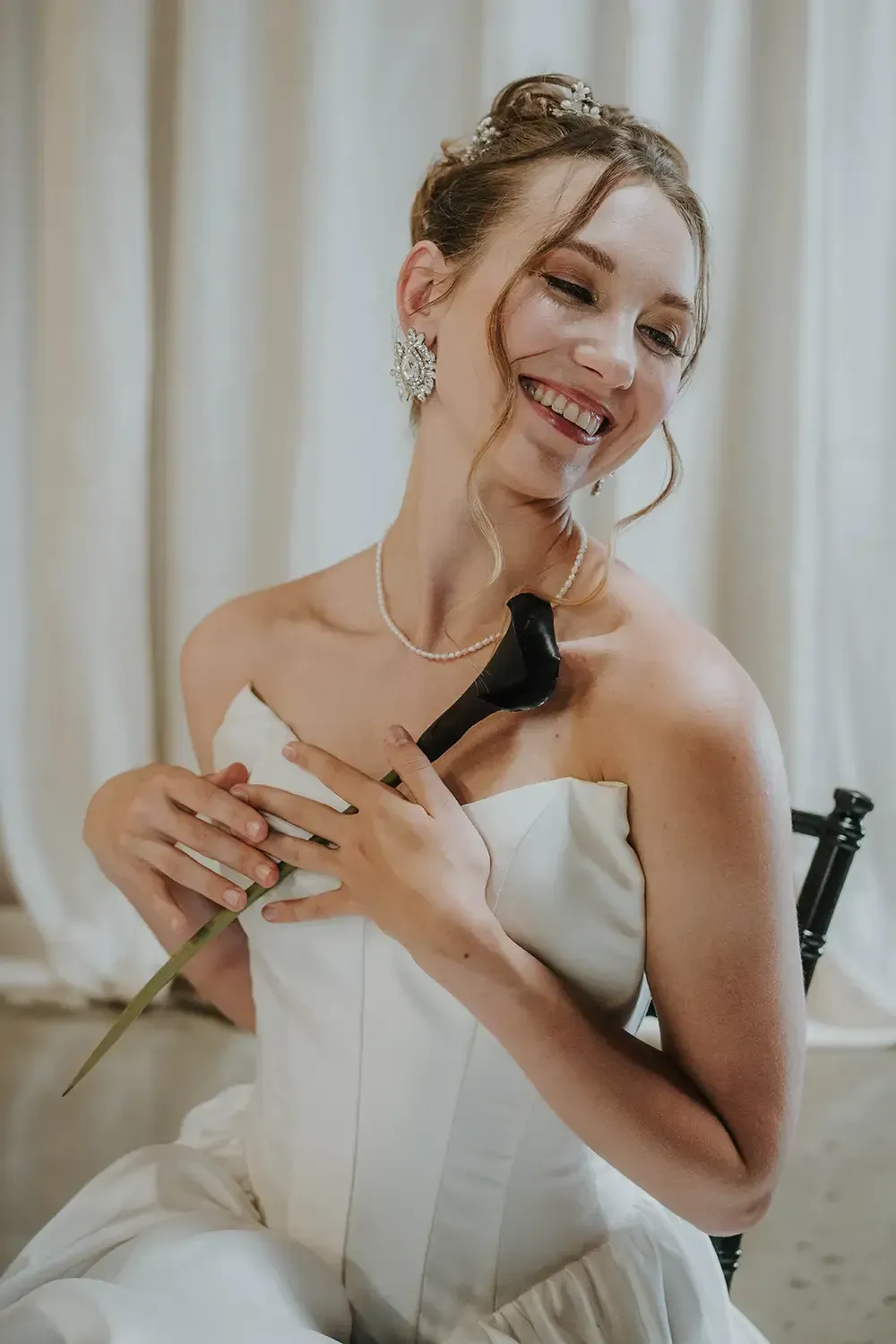 Smiling bride in a strapless white gown holding a lily
