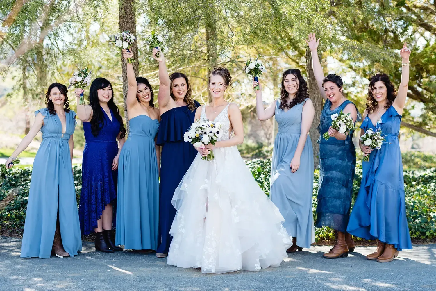 Bride and bridesmaids in blue dresses posing outdoors with soft glam hair and makeup