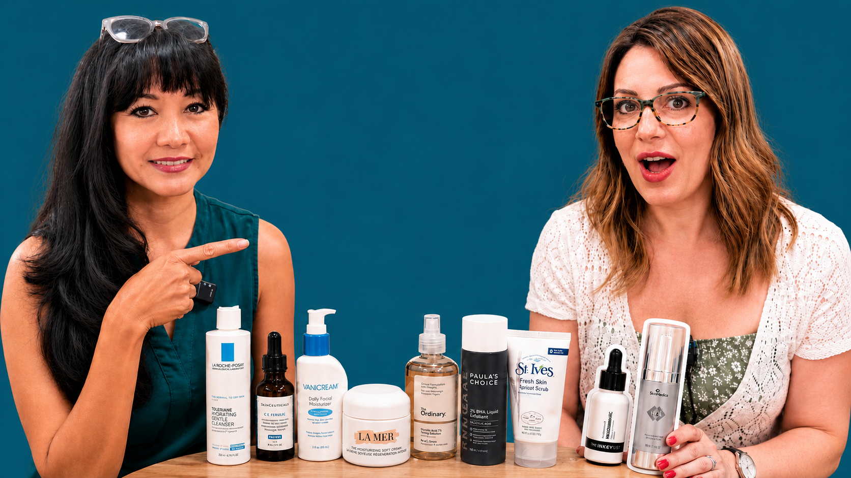 Two women pose with assorted skincare products on a table against a blue background.
