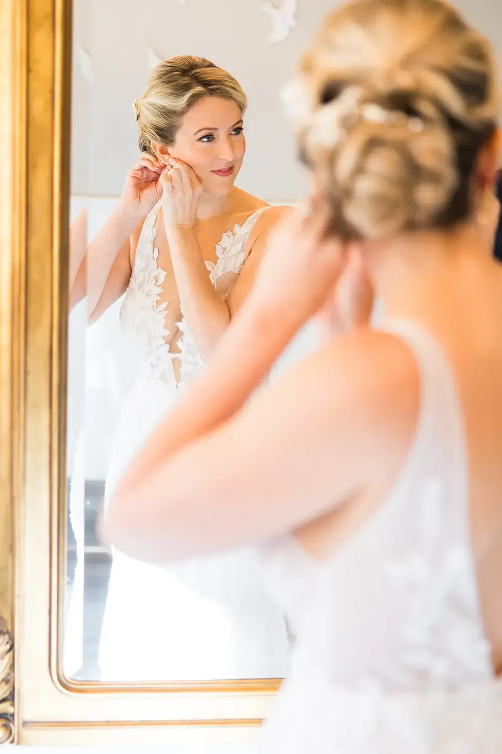 Elegant bride with updo and glowing makeup putting on earrings