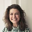 Smiling woman with shoulder-length dark hair in a patterned blouse against a light wall