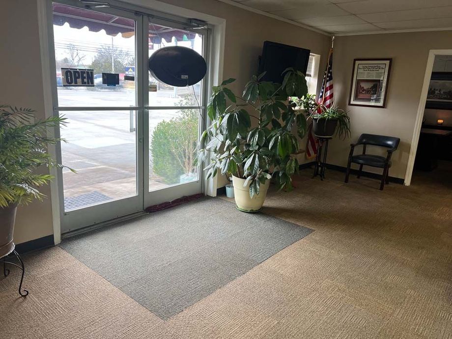 Lobby with glass entrance doors, carpeted floor, potted plants, and a chair in a waiting area.
