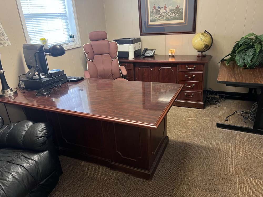 Office with a wooden desk, pink chair, drawers, globe, computer, and a black leather couch.