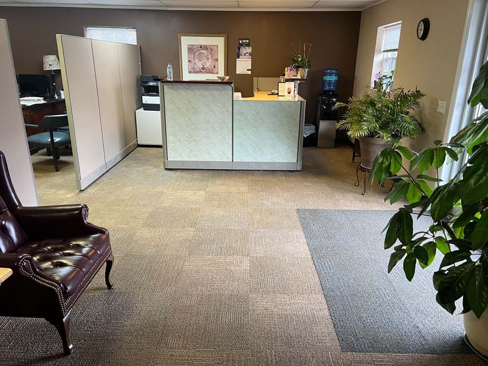 Empty office lobby with front desk, chairs, plants, and carpeted floor